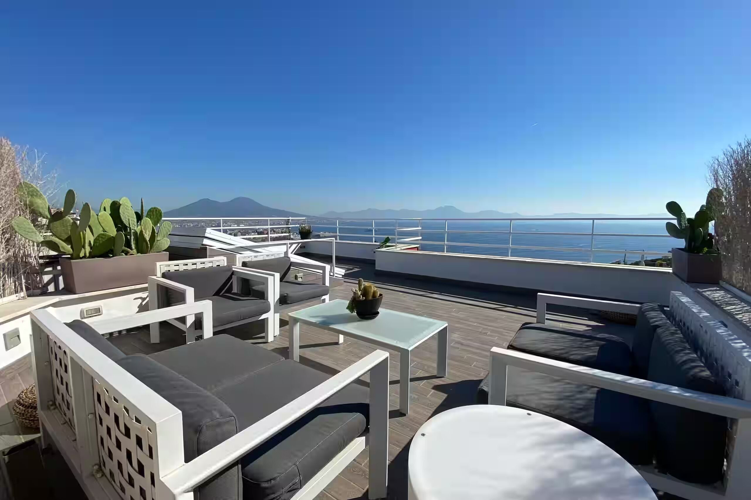 Une terrasse sur le toit, aménagée avec du mobilier d’extérieur, offrant une vue sur la mer et sur une montagne qui se profile à l’horizon.