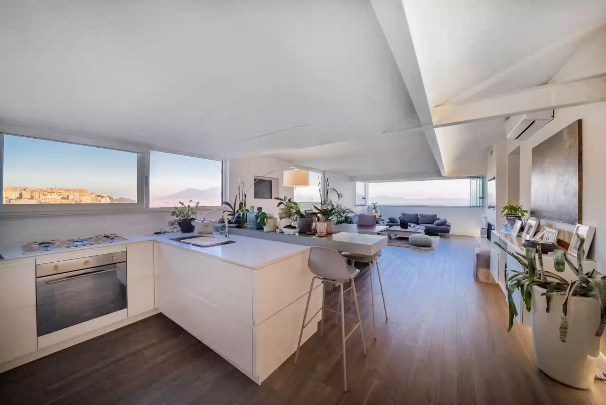 Une cuisine moderne dotée d’un îlot central, d’un coin repas avec un canapé et offrant une vue sur le paysage urbain et les montagnes.