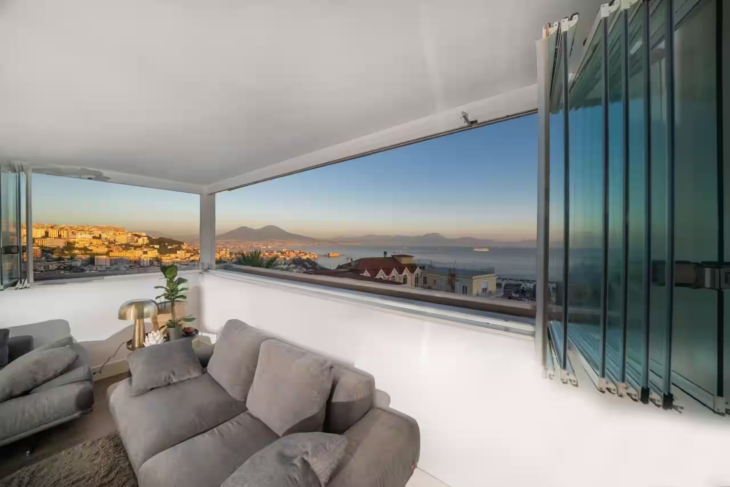 Un salon moderne doté d’une grande fenêtre donnant sur un paysage urbain et une montagne.