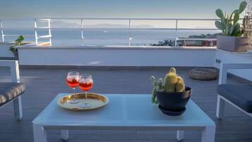 Una terrazza con un tavolo, due bicchieri di bevanda rossa, una pianta di cactus e vista sul mare.