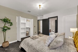 Ein Schlafzimmer mit Bett, Kleiderschrank, Pflanze und einer Badezimmertür.
