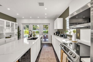Una cocina moderna con muebles blancos, estufa de acero inoxidable y una isla grande con pileta.