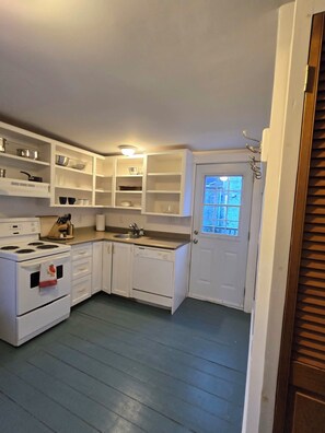 A compact kitchen with white cabinetry, a stove, and a window. - NEW LISTING Central Old Town Lunenburg Airy Loft Top Floor Apartment (Lunenburg)