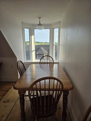 A dining room with a wooden table and chairs, large windows with a view of a house and landscape, and a ceiling fan. - NEW LISTING Central Old Town Lunenburg Airy Loft Top Floor Apartment (Lunenburg)