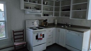 Une cuisine de taille réduite avec des meubles blancs, une cuisinière, un évier et une chaise.