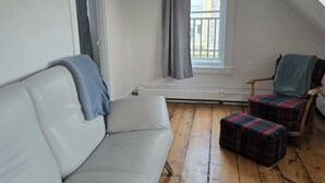 Une pièce avec un canapé blanc, un fauteuil à motifs écossais, une fenêtre donnant sur un beau paysage et un ventilateur de plafond.
