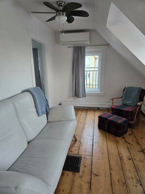 A room with a white sofa, a plaid armchair, a window with a view, and a ceiling fan.