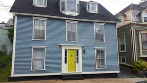 Une maison à deux étages avec une porte jaune vif, de nombreuses fenêtres et une cheminée.