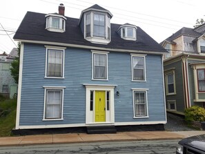 A two-story house with a bright yellow door, multiple windows, and a chimney.