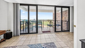 A room with a sliding glass door leading to an outdoor patio with chairs and a view of the landscape. - Aransas Princess #308, Family-Friendly Gulf-View 2BR/2BA Condo (Port Aransas)