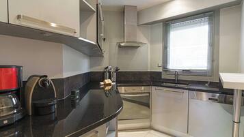 A modern kitchen with a black countertop, stainless steel appliances, and a window with blinds.