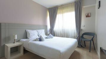 A hotel room with a bed, a nightstand, a chair, and a window with curtains.