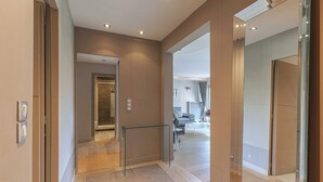 Moderni hotellikäytävä, jossa on lasikaide, näkyvissä oleva hissi sekä oleskelualue, jossa on sohva ja sohvapöytä.