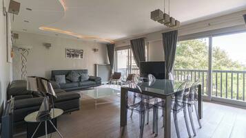 A modern living room with a glass coffee table, a sofa, and a dining area with chairs.