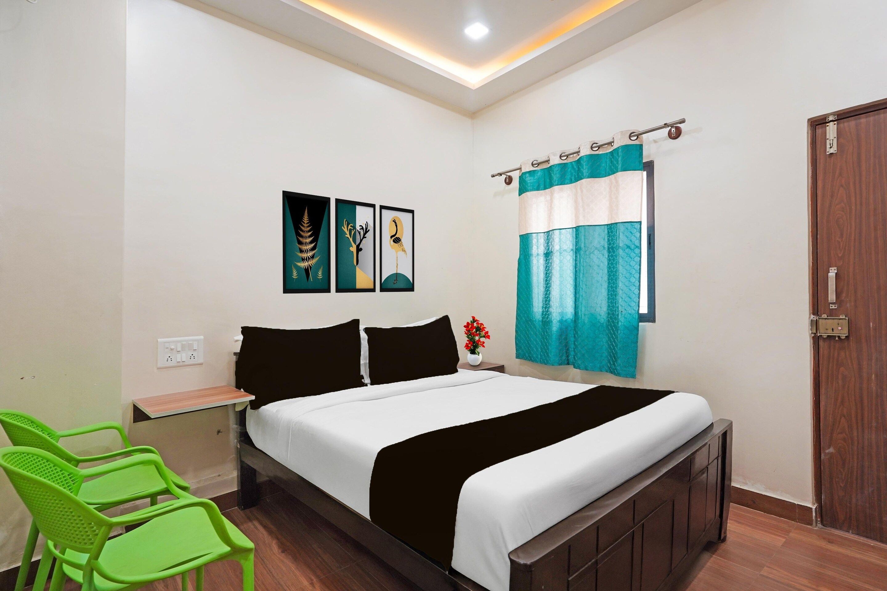 Une chambre à coucher avec un lit, une table de chevet, un fauteuil vert, une porte en bois et une fenêtre avec des rideaux.