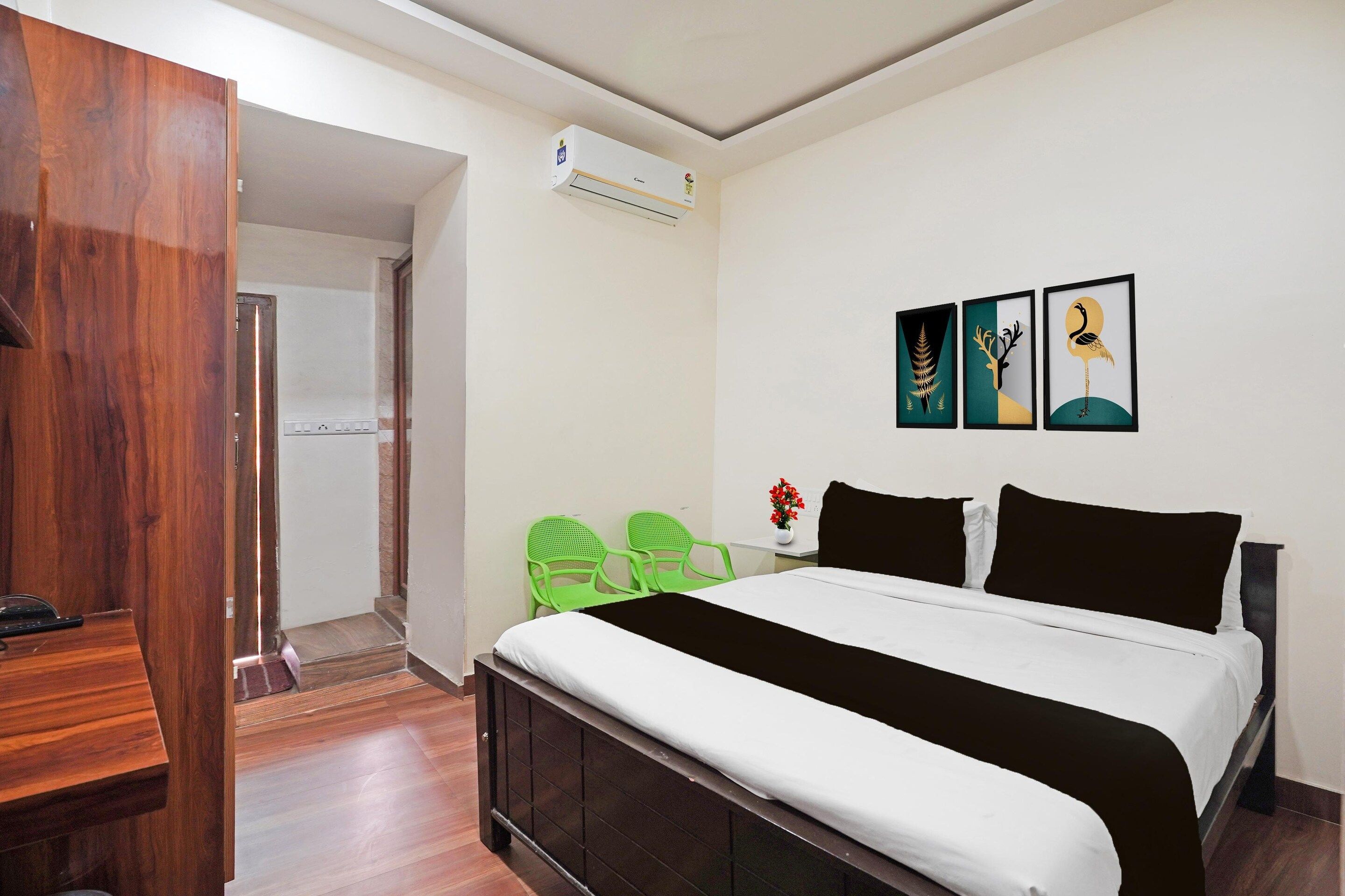 A hotel room with a bed, a desk, a chair, an air conditioning unit, and artwork on the wall.