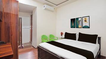 A hotel room with a bed, a desk, a chair, an air conditioning unit, and artwork on the wall.