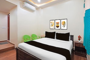A hotel room with a bed, two chairs, a nightstand, a wall-mounted air conditioner, and a framed artwork above the bed. - Collection O Thanisandra Bangalore (Bengaluru)