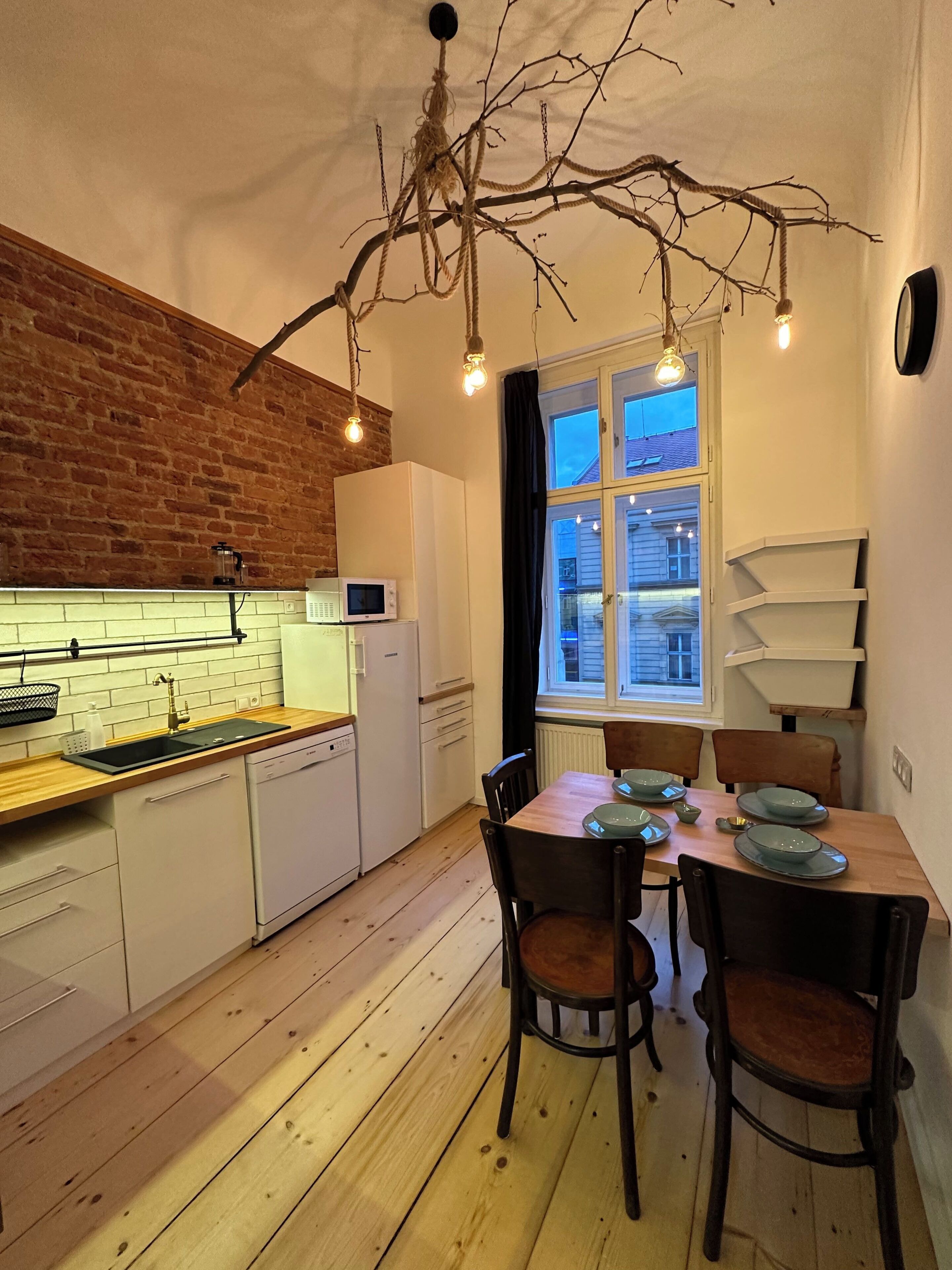 A kitchen with a wooden floor, white cabinets, a microwave, and a hanging light fixture.