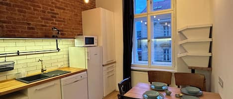 A kitchen with a wooden floor, white cabinets, a microwave, and a hanging light fixture.