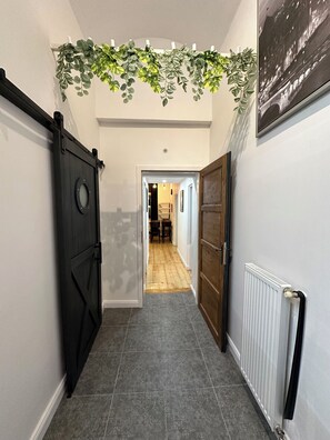 A hallway with a black sliding door, a radiator, and a hanging plant. - Modern Karlín Apt III Old Town Walk III Metro 1 Min (Hlavní město Praha)