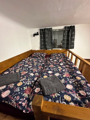 Un lit simple avec une couvre-lit à motifs floraux, une tête de lit en bois et une petite table de chevet en bois.