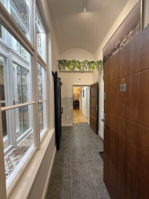 A hallway with a wooden door, a window with patterned glass, and a hanging plant. - Modern Karlín Apt III Old Town Walk III Metro 1 Min (Hlavní město Praha)
