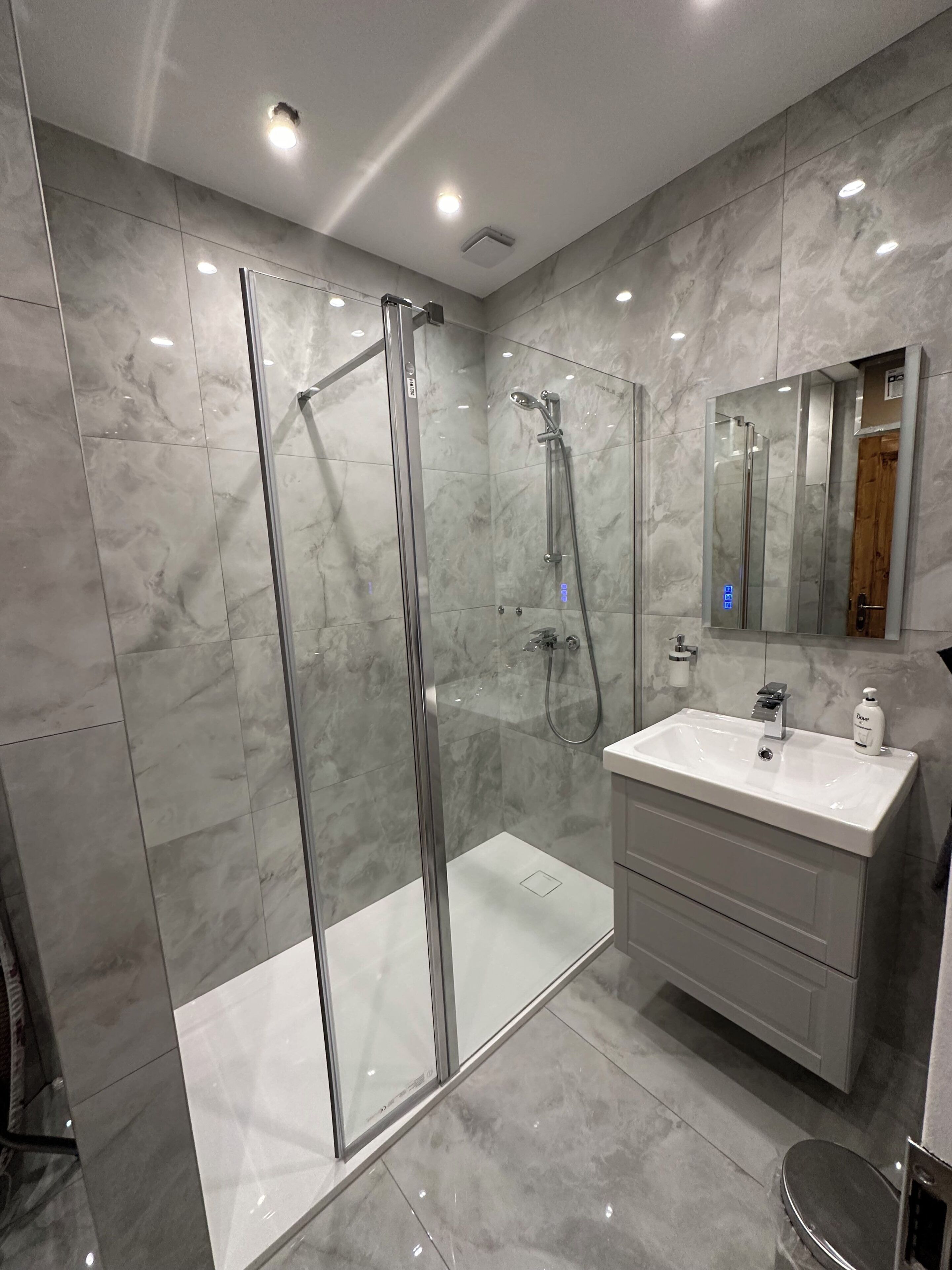 A modern bathroom with a glass-enclosed shower, a white vanity with a mirror, and marble flooring.