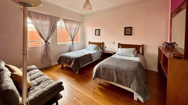 Un dormitorio con dos camas, una mesita de noche, una lámpara, un espejo y una ventana con cortinas.