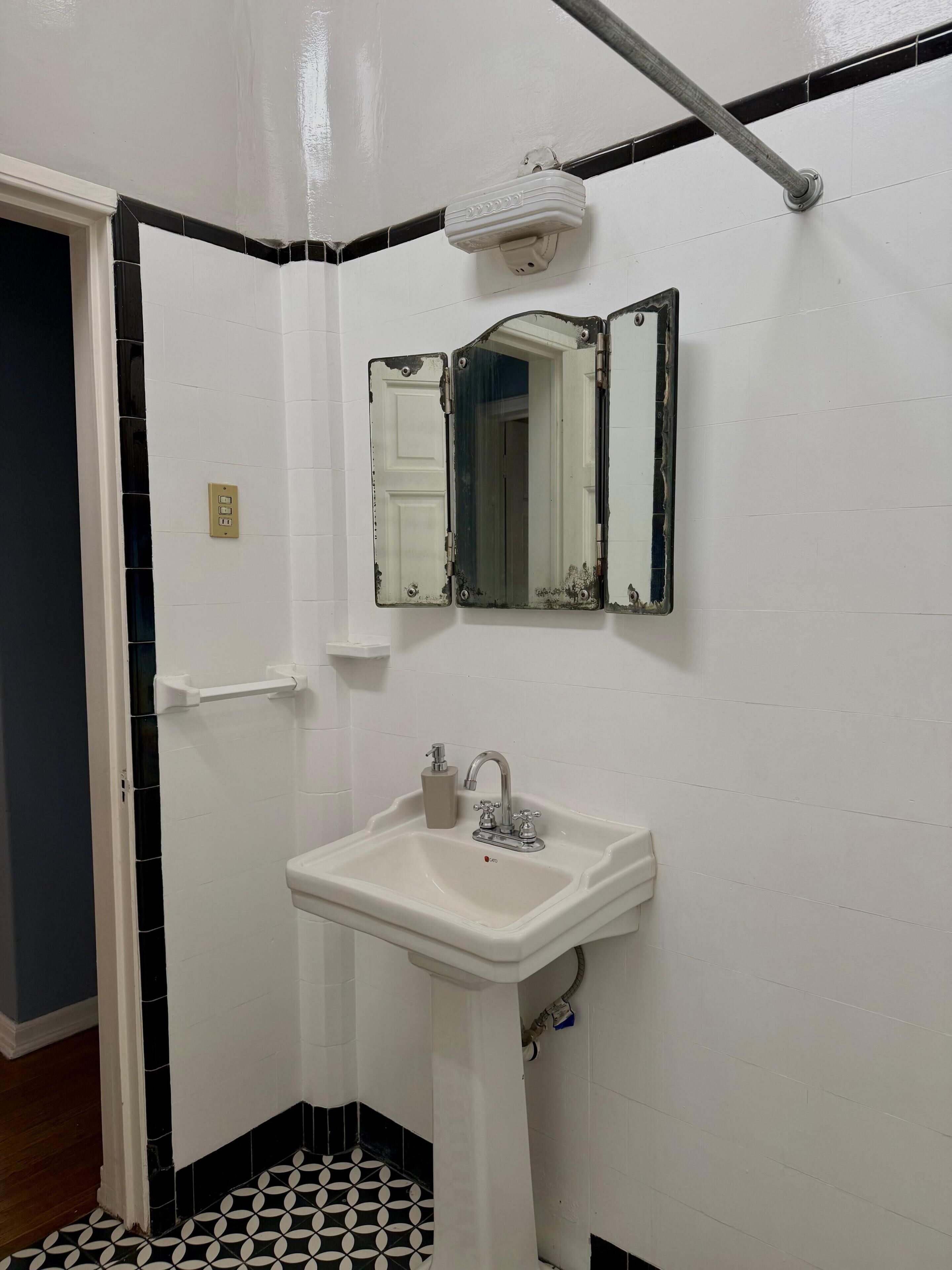 Un bagno con un lavandino bianco, uno specchio e una porta.