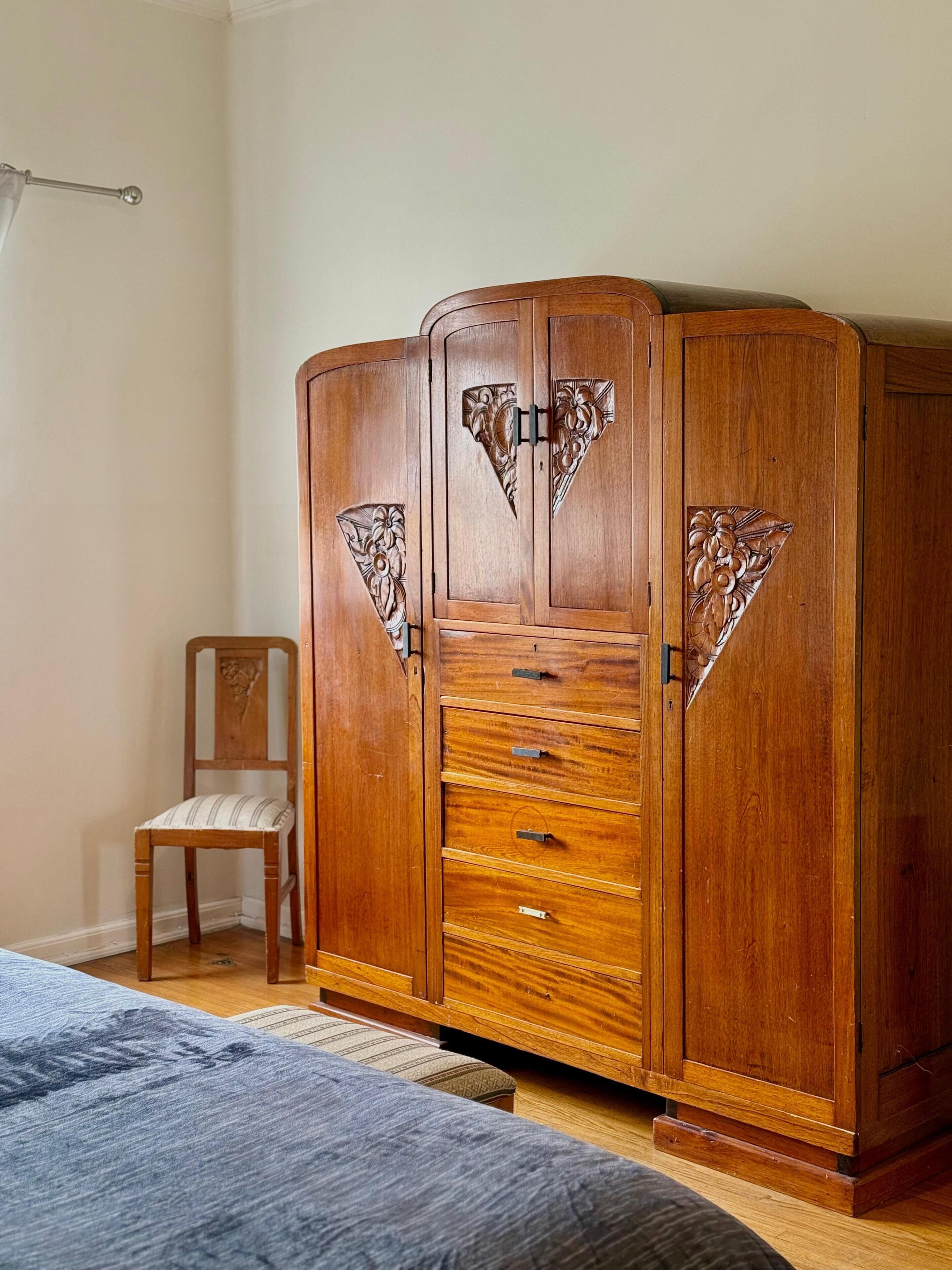 A bedroom with a wooden wardrobe, a chair, and a bed.