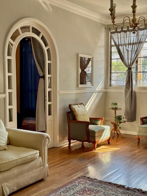 A room with a wooden floor, a beige sofa, a chair, a small table with a plant, and a window with curtains. - Central House with 5 Bedrooms & Double Garage (Heroica Puebla de Zaragoza)
