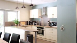 A modern kitchen with a central island, built-in appliances, and a dining area with chairs. - Air-conditioned Gîte "La Maison du Parc" with Private Pool near Nuits-Saint-Georges (Argilly)