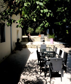 An outdoor patio with a table and chairs, surrounded by greenery and a stone wall.