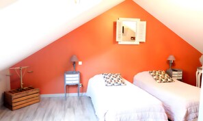 Ein Zimmer mit zwei Betten, einer hölzernen Truhe, einem Nachttisch mit Lampe und einem Wandspiegel.