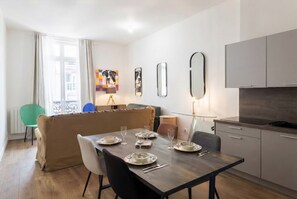 A modern living space with a dining table set for four, a sofa, a kitchen area, and a view of the city. - celine 36 (Paris)