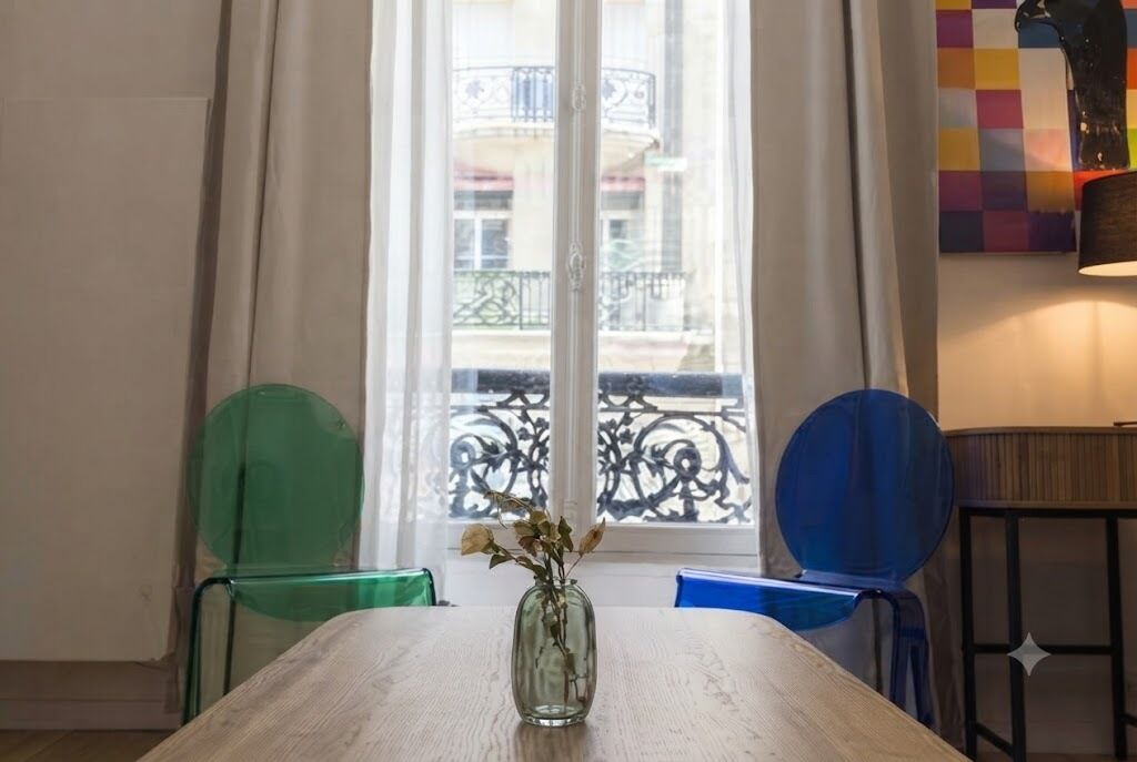 A room with a wooden table, a vase with flowers, and a view of a balcony with a railing.