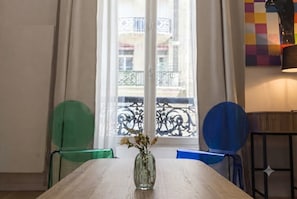 A room with a wooden table, a vase with flowers, and a view of a balcony with a railing. - celine 36 (Paris)