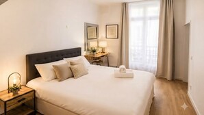 Hotellihuone, jossa on suuri sänky, yöpöytä, lamppu ja ikkunasta avautuva näkymä ulos.