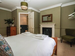 Ein Schlafzimmer mit Bett, Kommode, Stuhl, Kamin und Spiegel an der Wand.