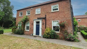 A two-story brick house with a blue door, white windows, and a small garden with various plants and flowers. - Kexby House (York)