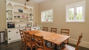 A kitchen with a wooden table and chairs, white cabinetry, and a window with a view of greenery. - Kexby House (York)