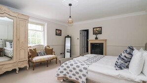 A bedroom with a large bed, a wardrobe, a chair, a mirror, and a fireplace. - Kexby House (York)
