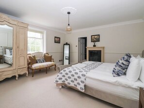 Ein Schlafzimmer mit einem großen Bett, einem Kleiderschrank, einem Sessel, einem Spiegel und einem Kamin.