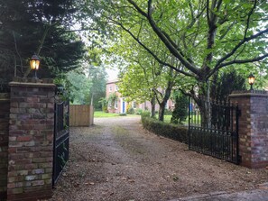 A gated entrance with brick walls and metal gates, leading to a building with a brick facade and a blue door. - Kexby House (York)