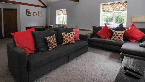 A living room with a dark grey sofa set, red and patterned cushions, a coffee table, and a window with a view of greenery. - Kexby House (York)
