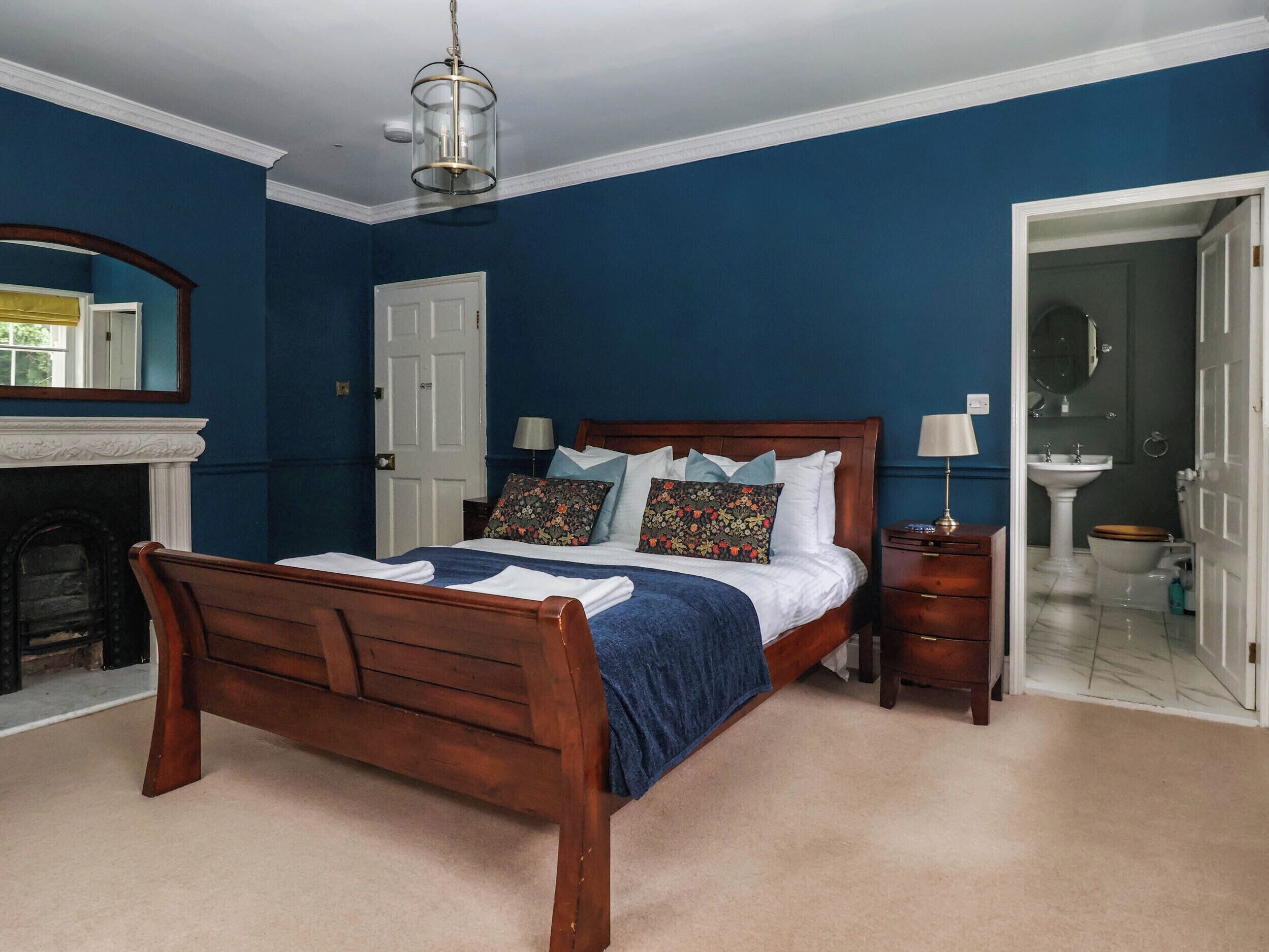 A bedroom with a wooden bed, a white door, a mirror, and a bathroom visible through an open door.