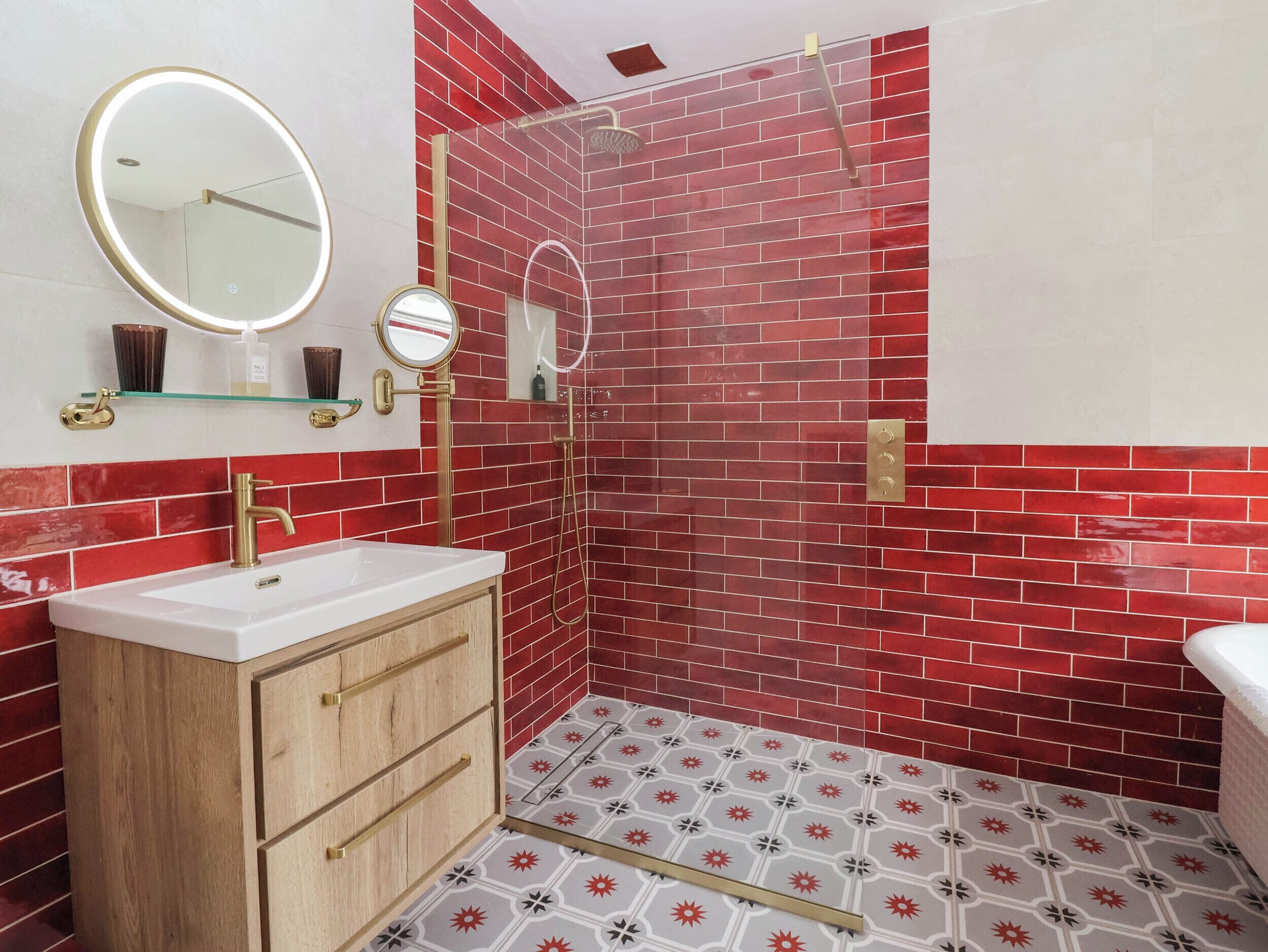 A bathroom with a red-tiled shower, a white sink with gold fixtures, and a mirror with a gold frame.