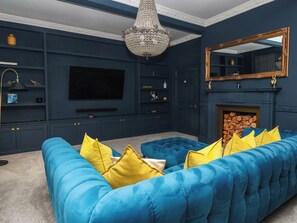 Ein Wohnzimmer mit einem großen blauen Sofa, einem Flachbildfernseher, einer Kristallleuchtre und einem Kamin.
