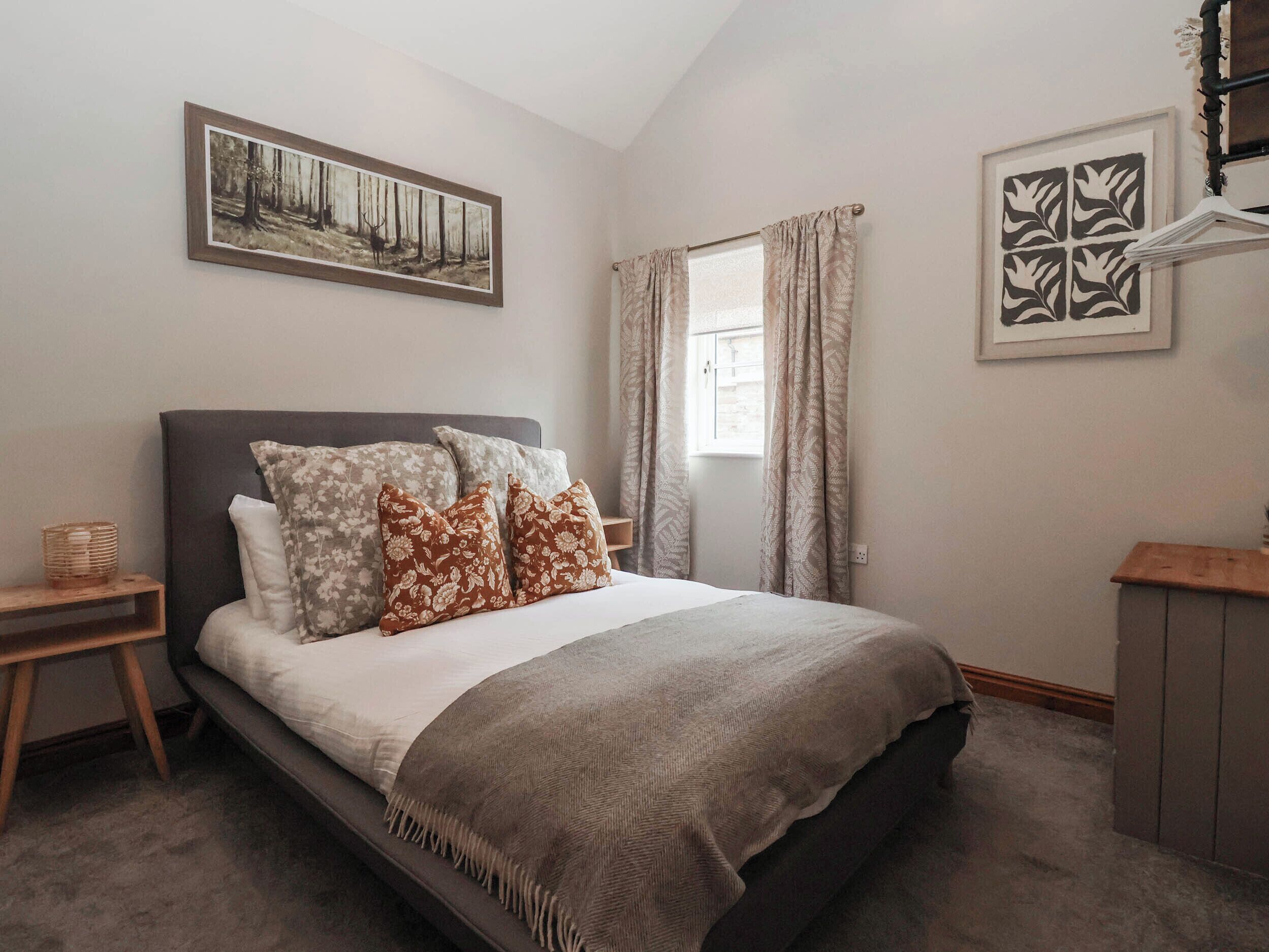 A bedroom with a bed, a nightstand, a window with curtains, and a wall-mounted picture.